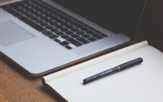 Laptop, buku catatan, dan pena di atas meja kerja